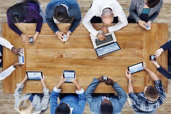 People around a boardroom table on their phones and laptops